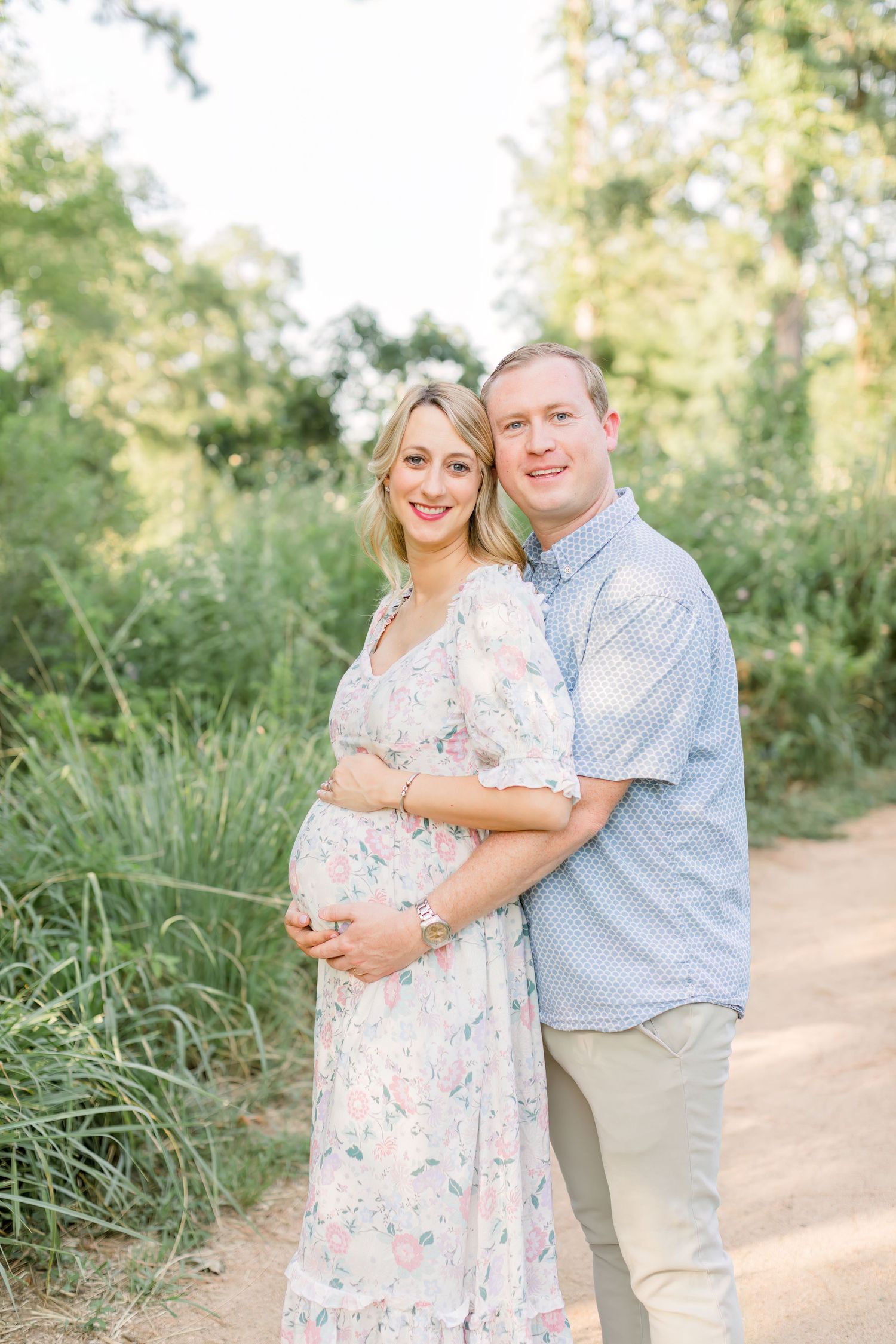 A joyful maternity portrait of a couple on a sunlit nature path.