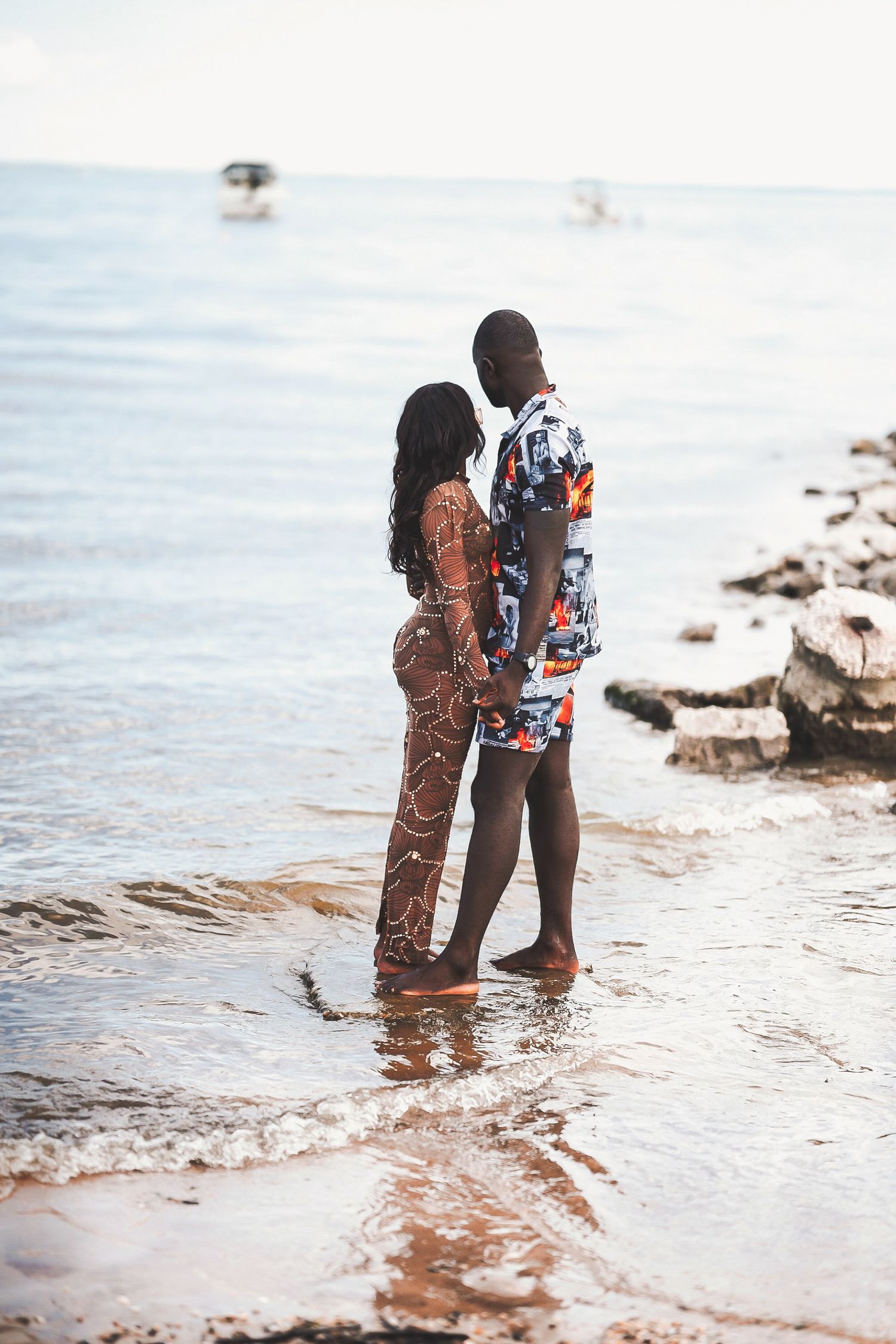 Romantic couple standing in shallow ocean water wearing patterned outfits.