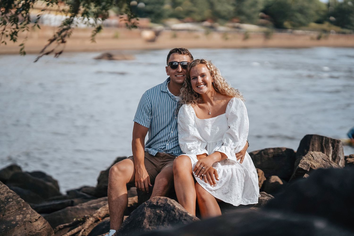 Couple sitting together on coastal rocks with water view in background.