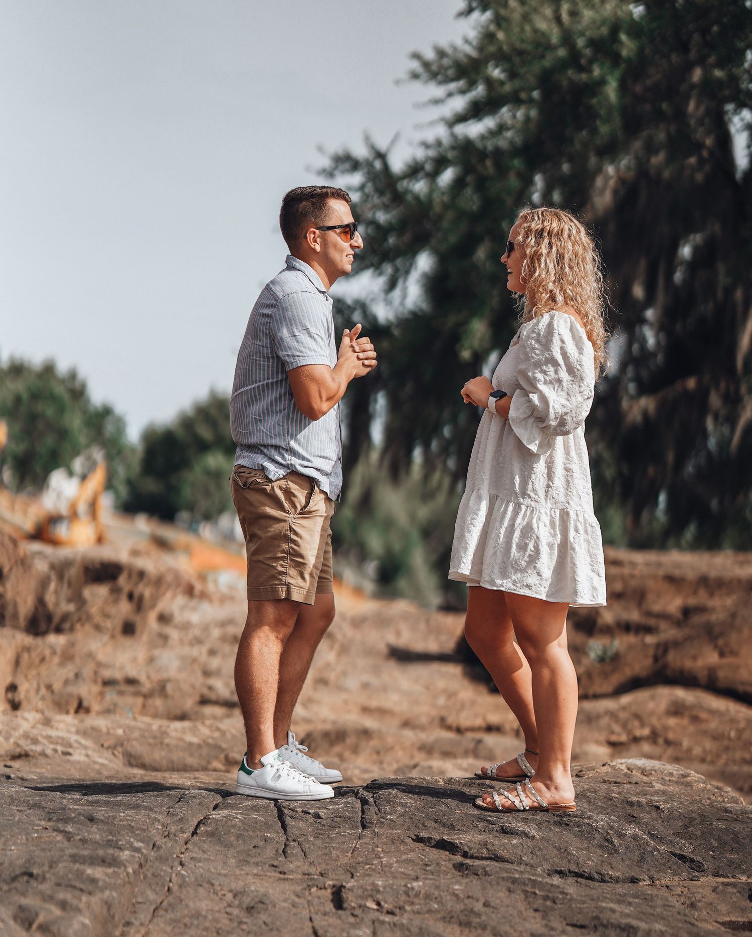 Couple sharing a moment on rocky shoreline in casual summer outfits.