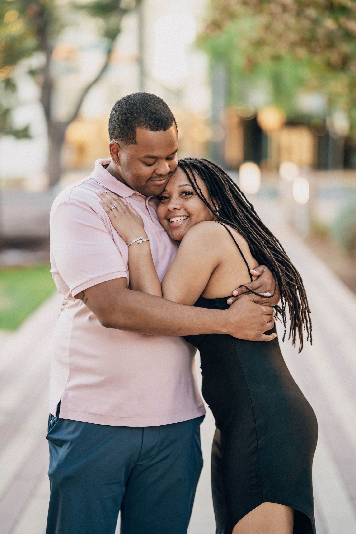 A loving couple embraces on a tree-lined path.