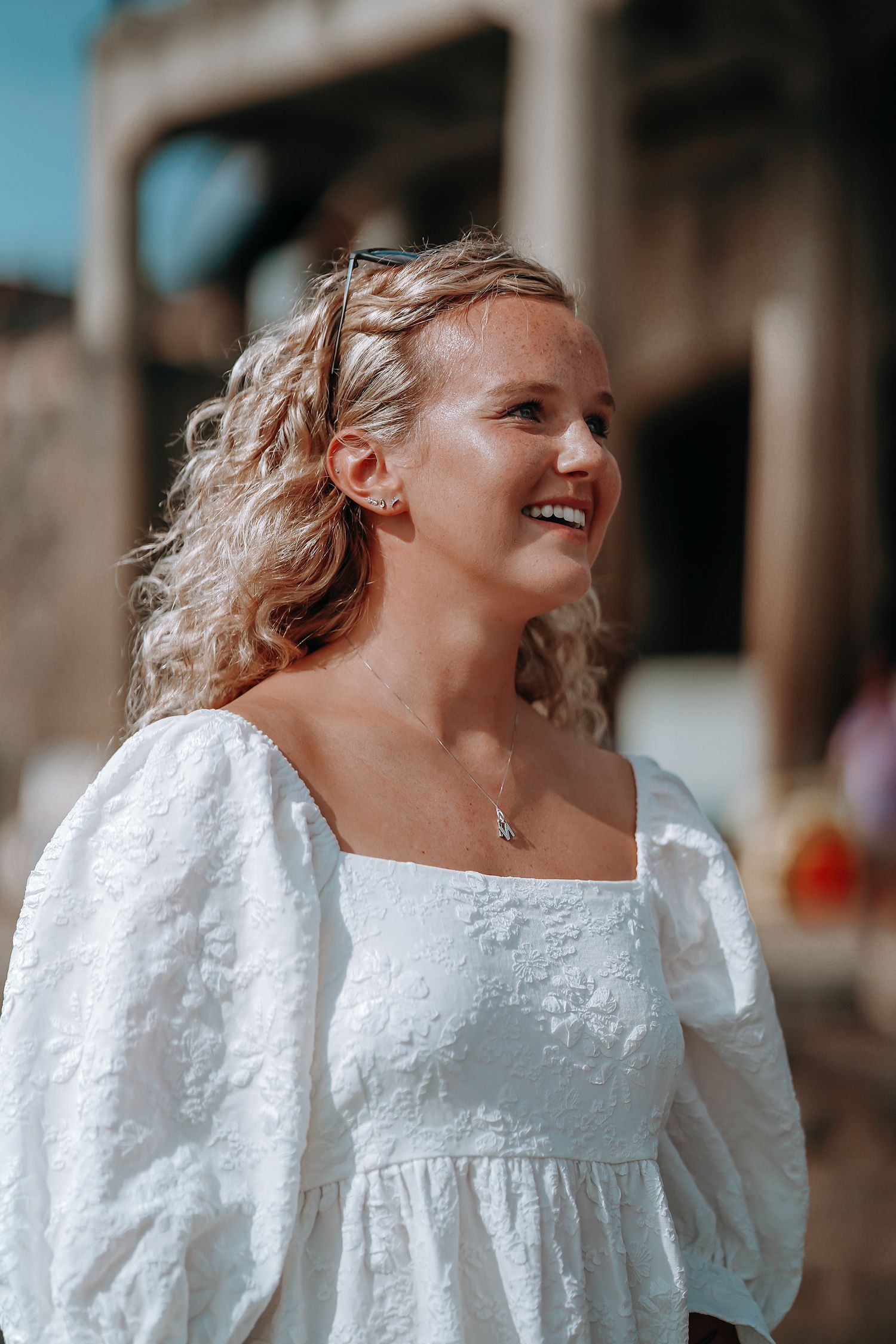 A woman in a white eyelet dress smiles brightly outdoors.