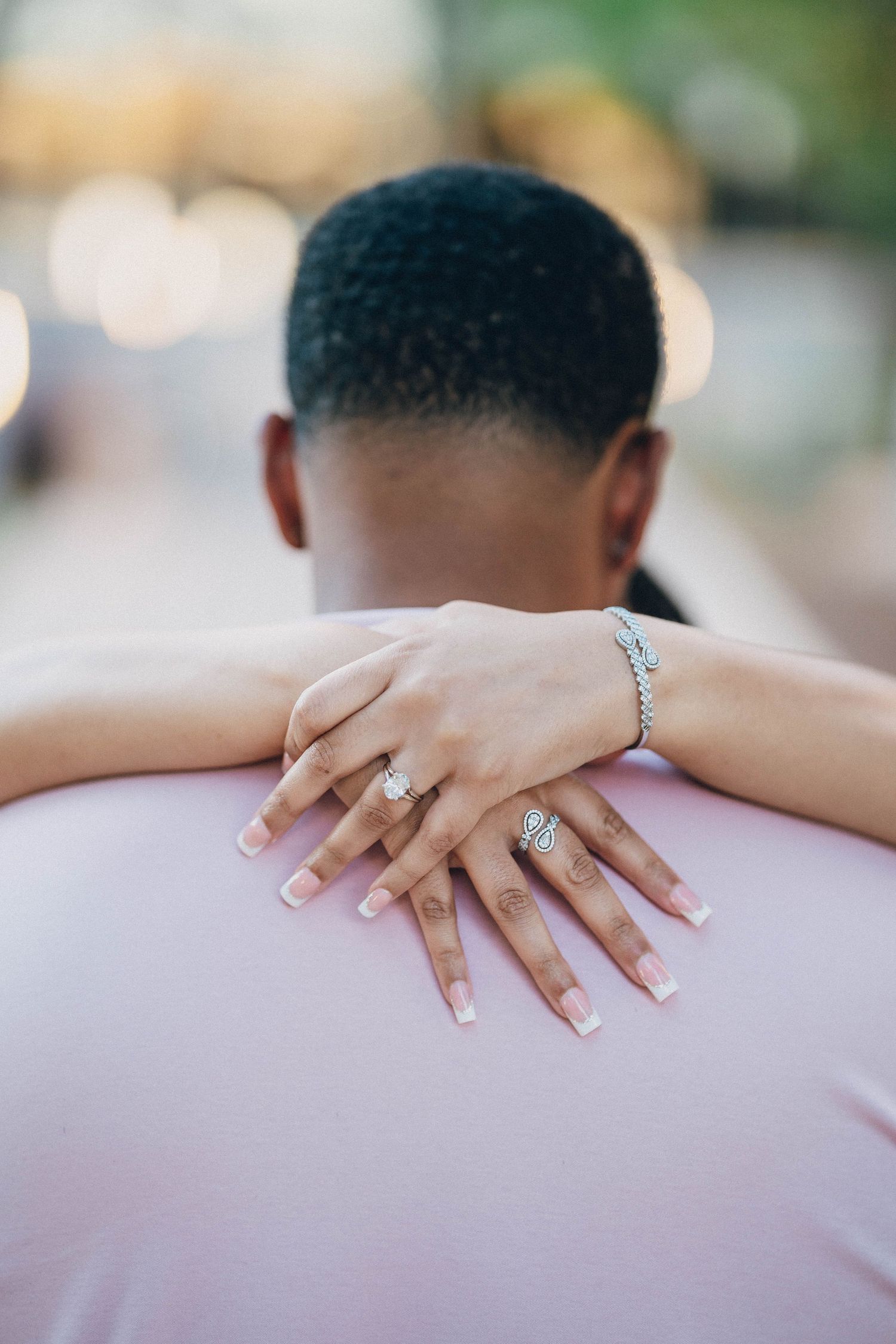 Close-up of hands with engagement ring resting on shoulder.