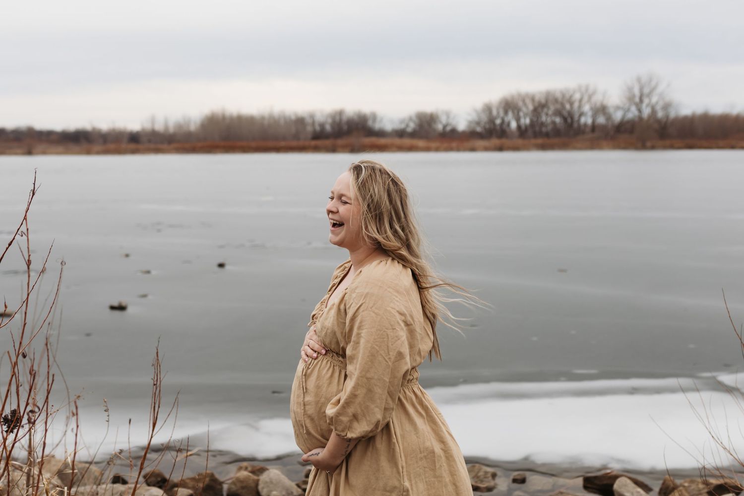 Someone in a beige coat standing by a frozen lake on a winter day.