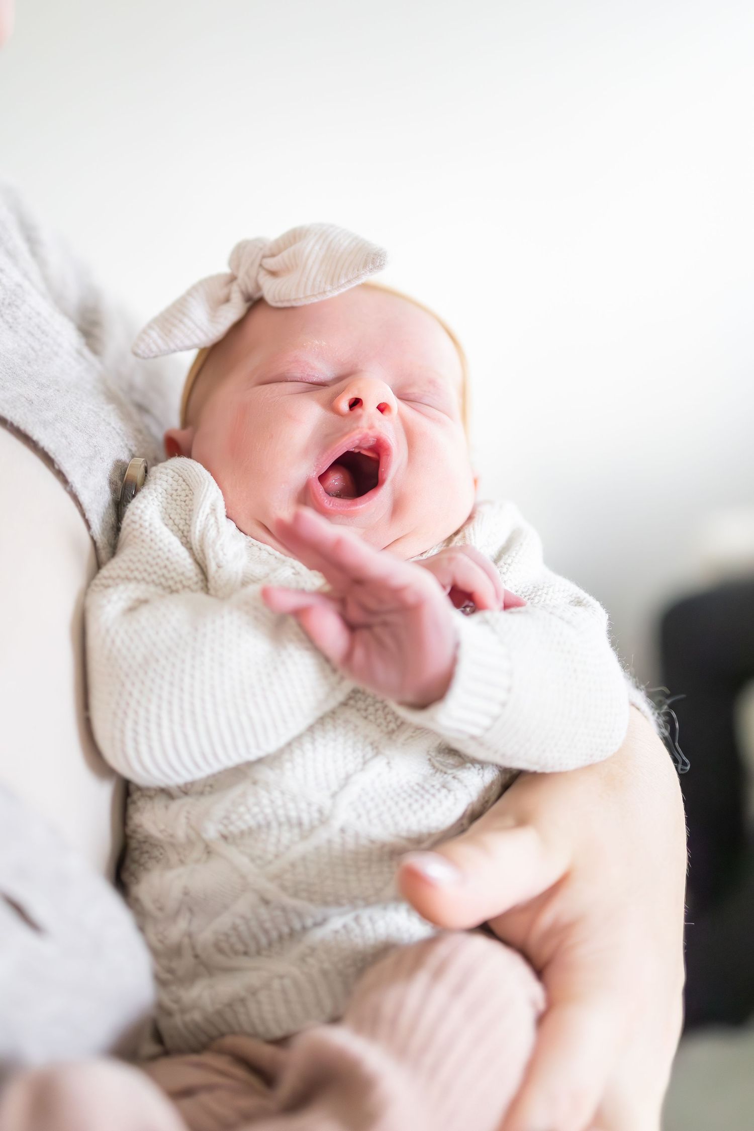 Baby in white knit sweater yawning while being held.