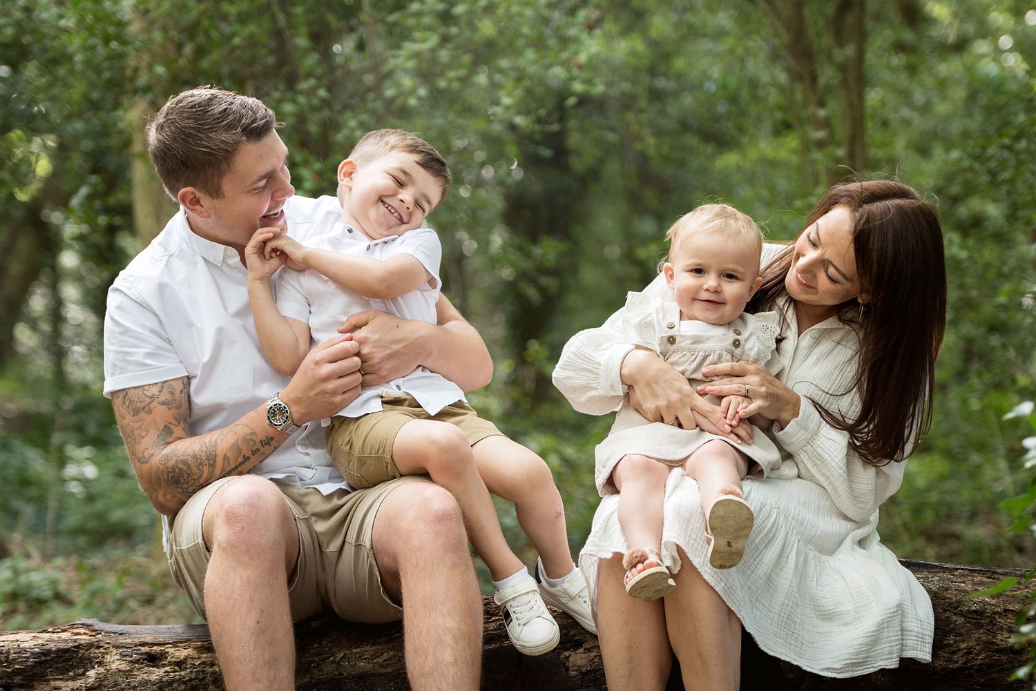 A family of four shares a tender moment while sitting on a log in the woods.