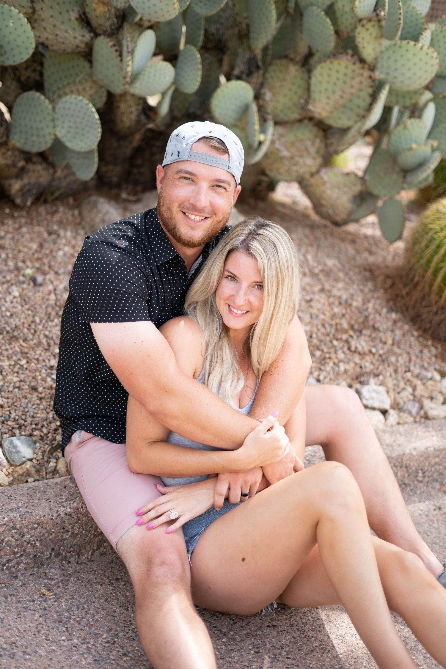 A couple poses casually together near desert cacti in warm summer attire.