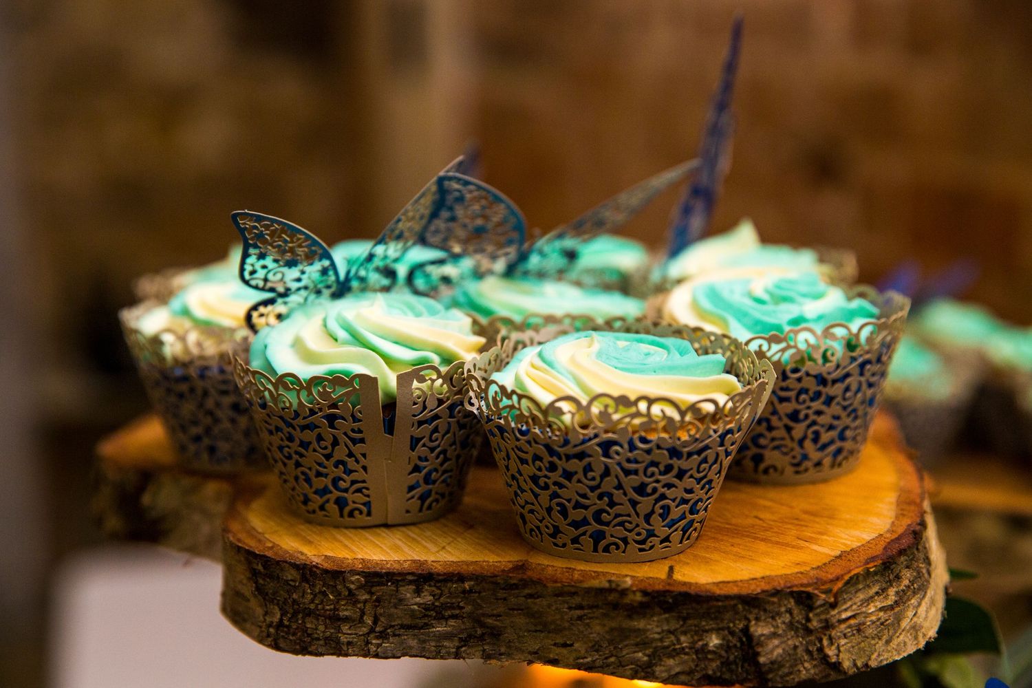Decorative cupcakes with mint green frosting displayed on wooden slices at a rustic wedding reception.
