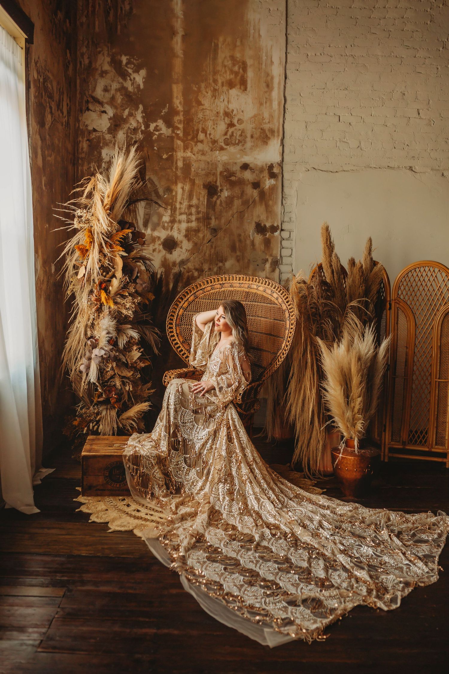 Ethereal bridal portrait with long lace train surrounded by dried flowers and peacock chair.