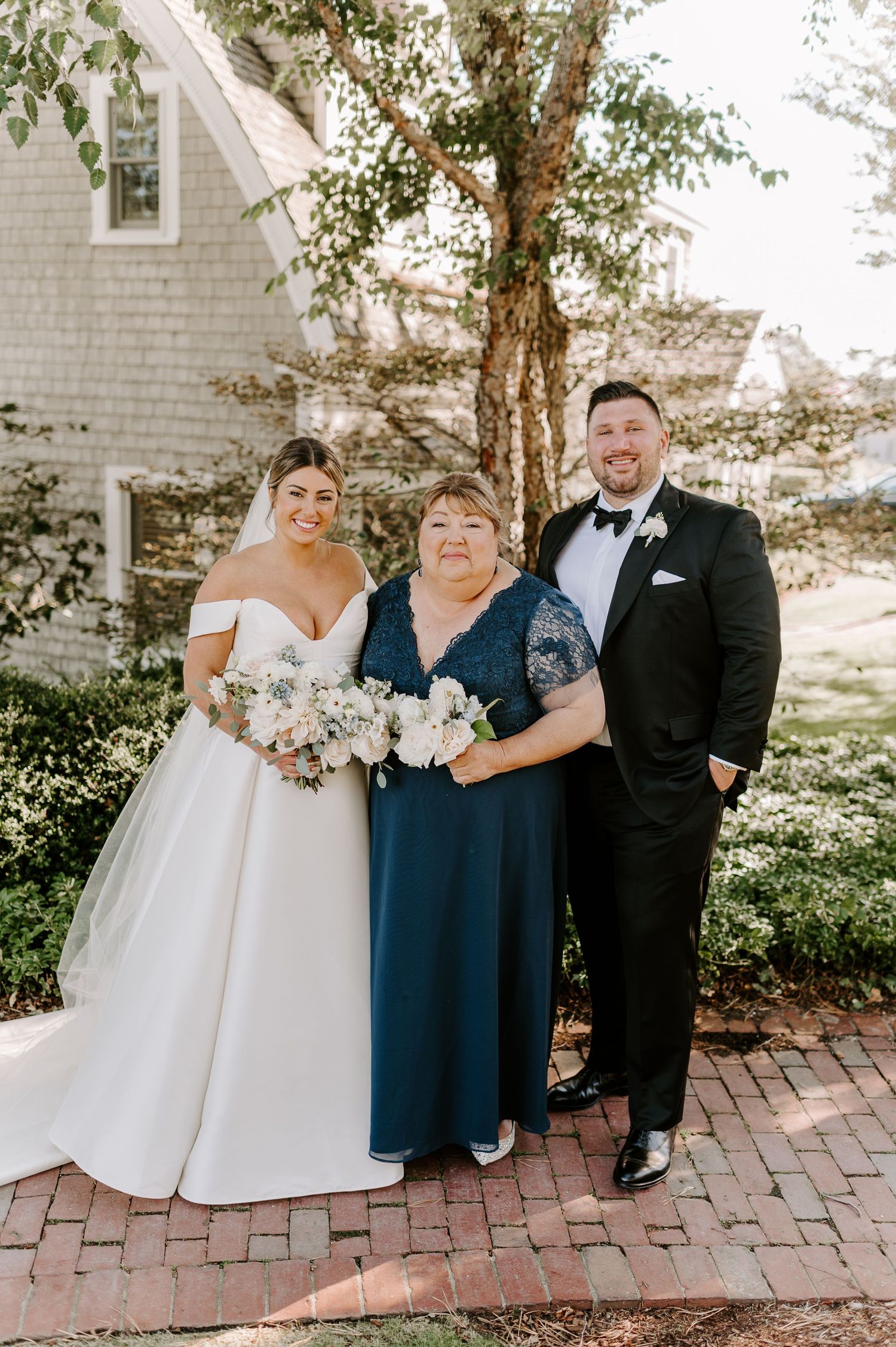 Wedding party members pose for formal portraits on brick pathway near white building.