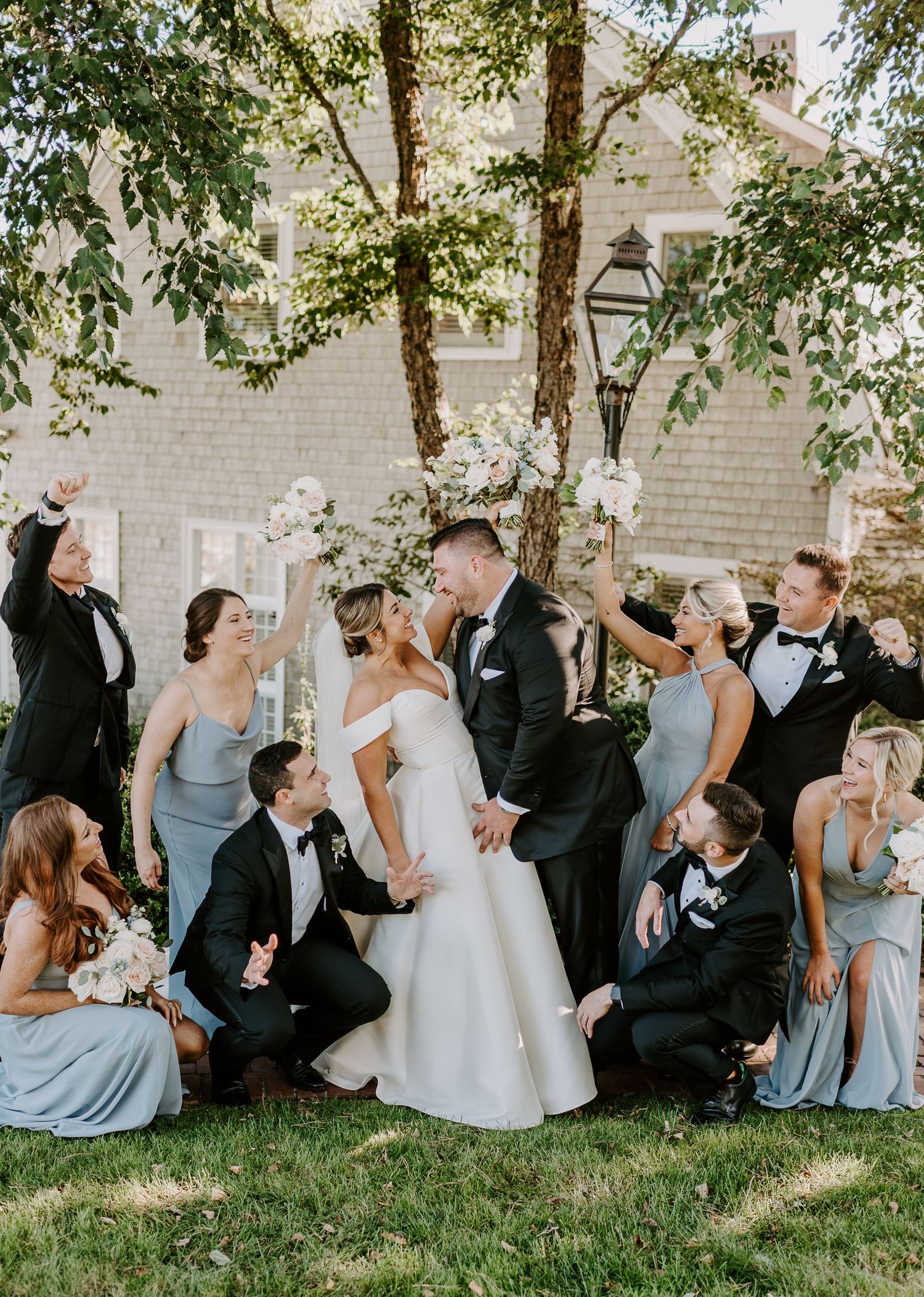 Wedding party sits on grass having fun and laughing during casual photo session.