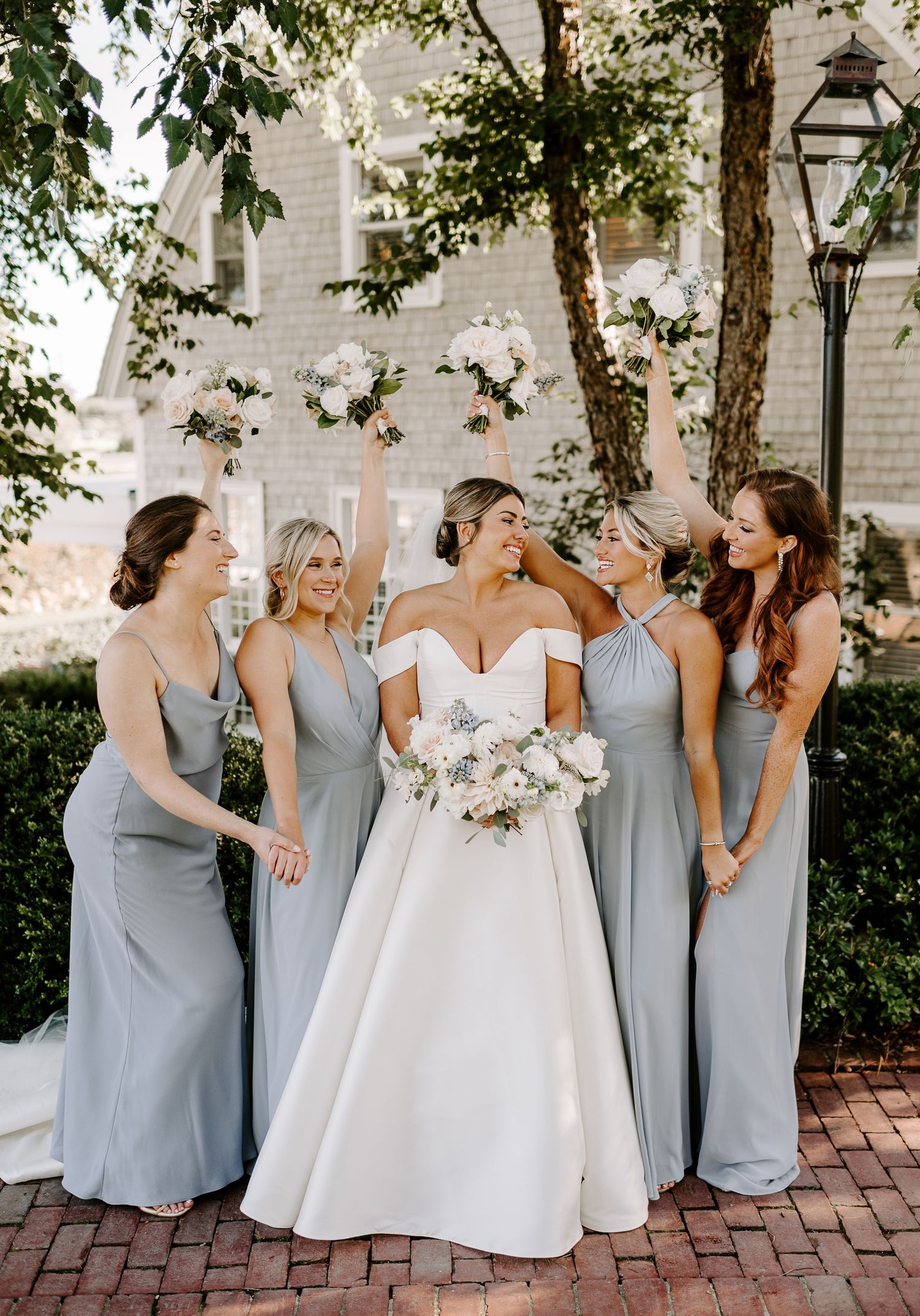 Bridesmaids in gray dresses laugh together during outdoor wedding photo session.