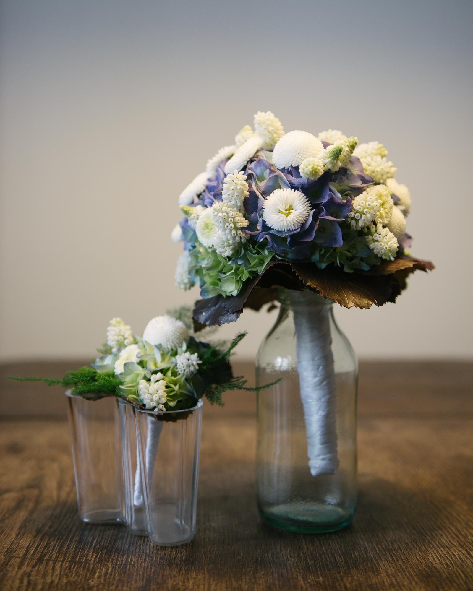 Elegant wedding bouquet arrangement with blue and white flowers in glass vases on wooden table.