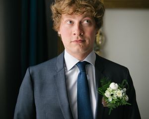 Person in formal attire with boutonniere looking to the side.
