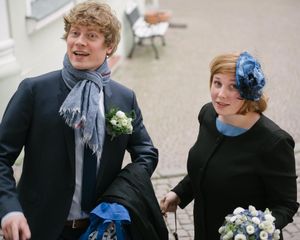 Two people in formal wear with bouquets and blue accessories walking together.