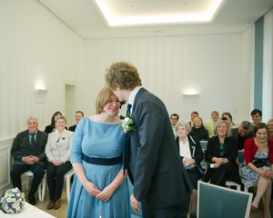 A wedding ceremony in a modern white room with minimalist decor and guests seated watching the couple.