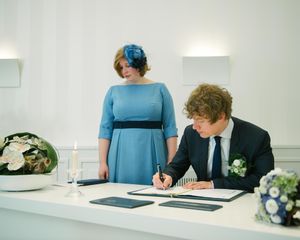 A couple at a wedding signing ceremony in a modern white room with blue accents.