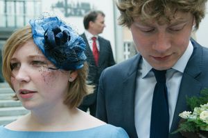 A couple in formal attire with a decorative blue headpiece and floral boutonniere.
