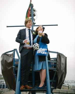 A couple in formal attire standing on a boat platform against an overcast sky.