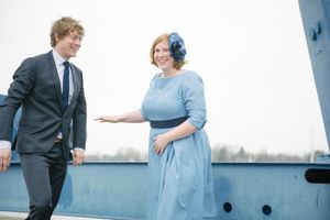 A stylish pair engaged in conversation on a boat deck with industrial equipment visible.