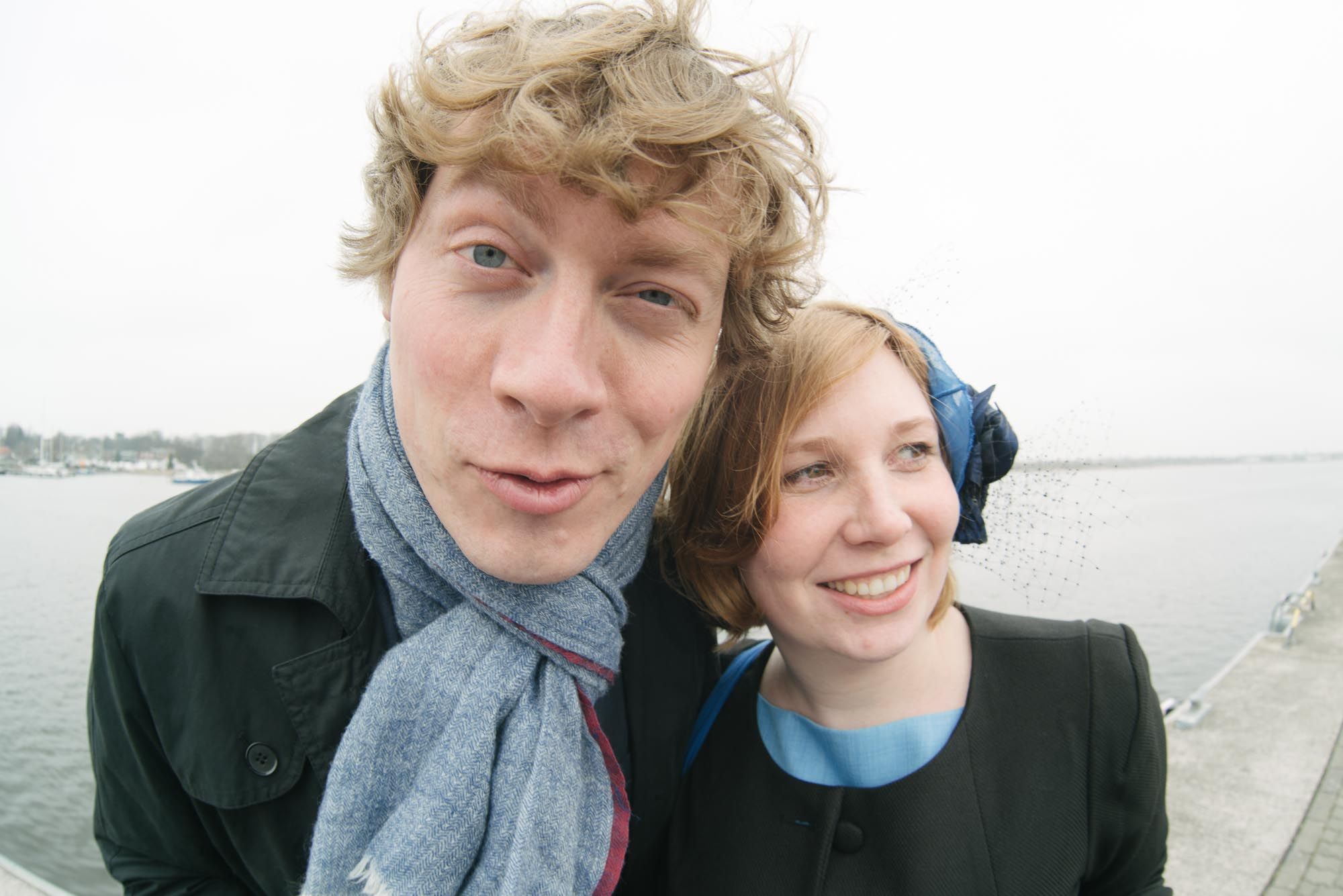 A close-up selfie portrait taken outdoors with maritime scenery in the background.