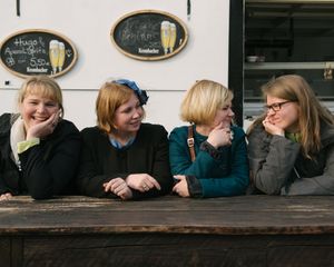 Four friends sharing a laugh while sitting at a wooden bench outdoors.