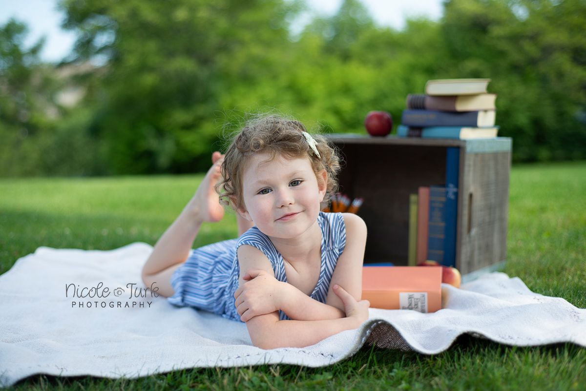 young school age girl lays on tummy outdoors with her school books