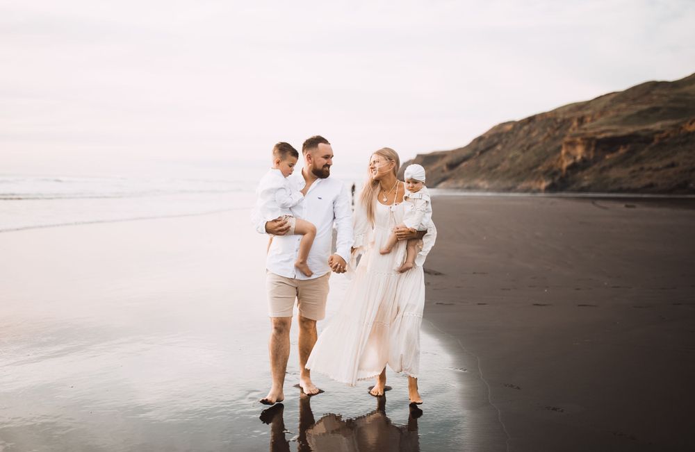 Family members stand together on dark sandy beach at sunset.
