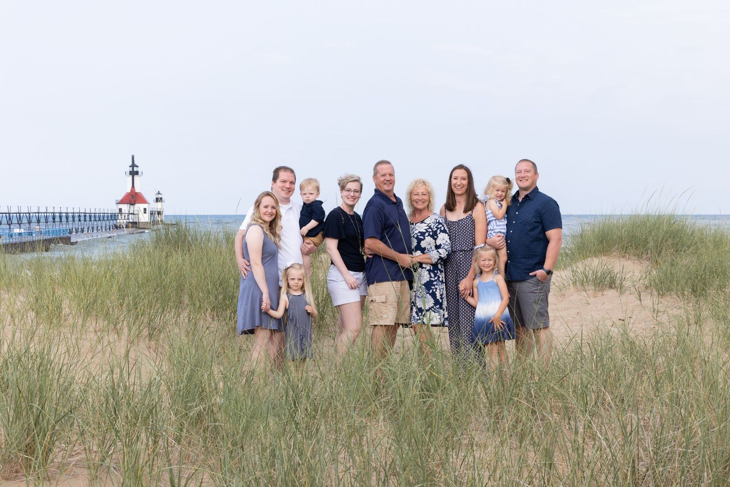 Family group portrait on grassy dunes with lighthouse in background at sunset.