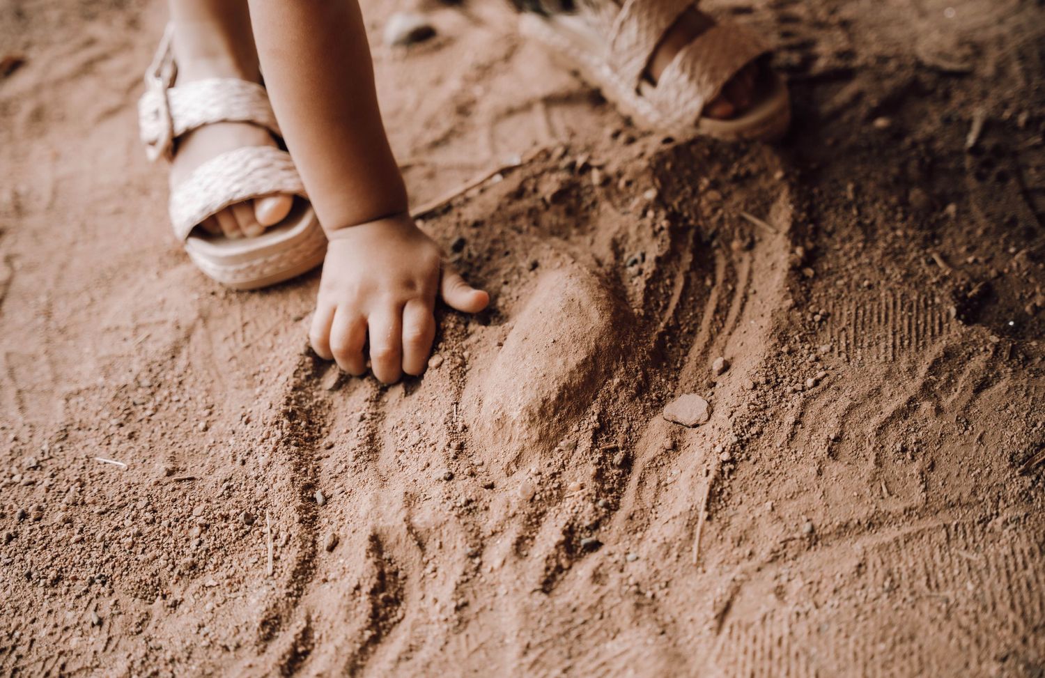 A child's hand and foot play in textured sand, creating natural patterns and impressions.