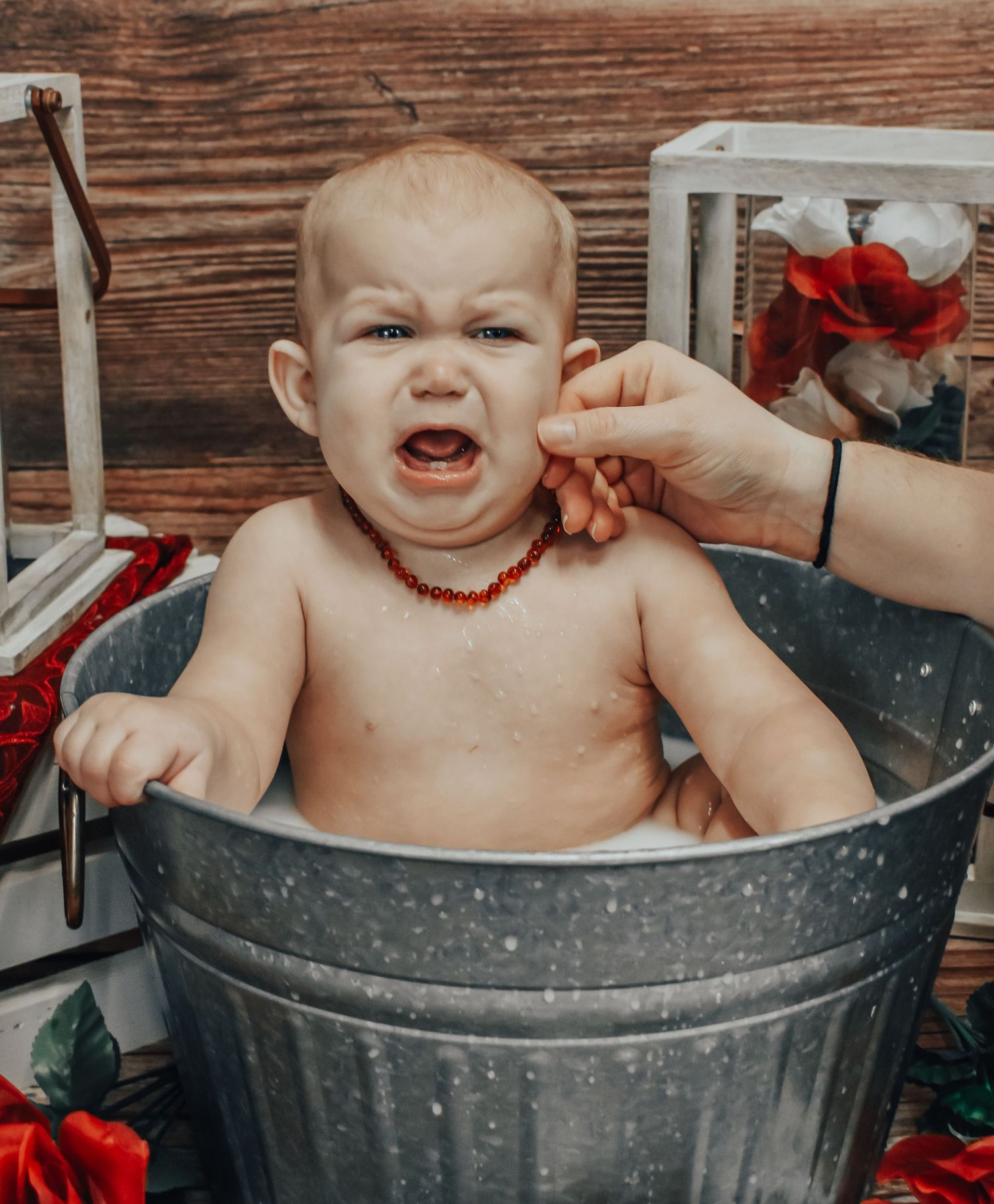 Baby sits in metal washtub during playful bath time photoshoot with rustic wooden background.