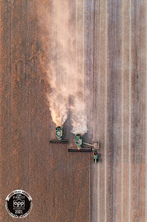 Aerial view of three harvesters kicking up dust while working in parallel on farmland.