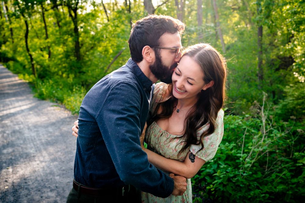 A romantic moment captured between a couple on a sunlit forest path.