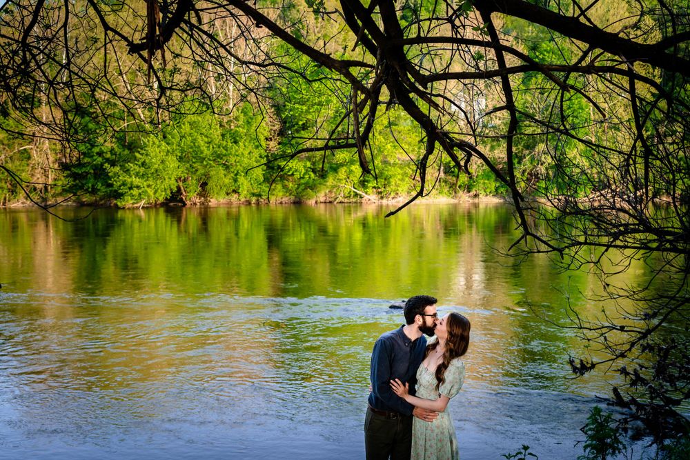 A couple shares a romantic moment by a serene lake with overhanging tree branches.