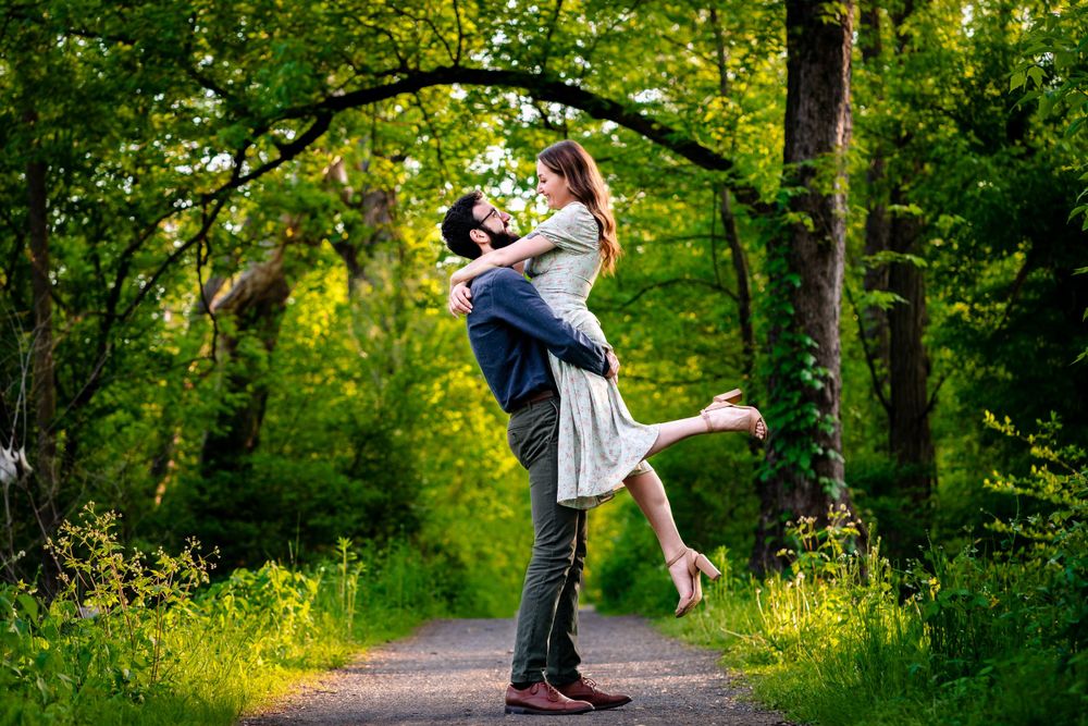 A couple shares joyful moments together on a sunlit forest path.