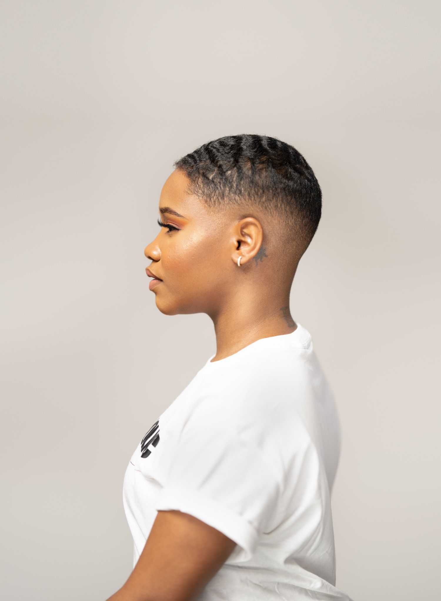 Profile portrait showcasing short textured haircut and white t-shirt against neutral background.