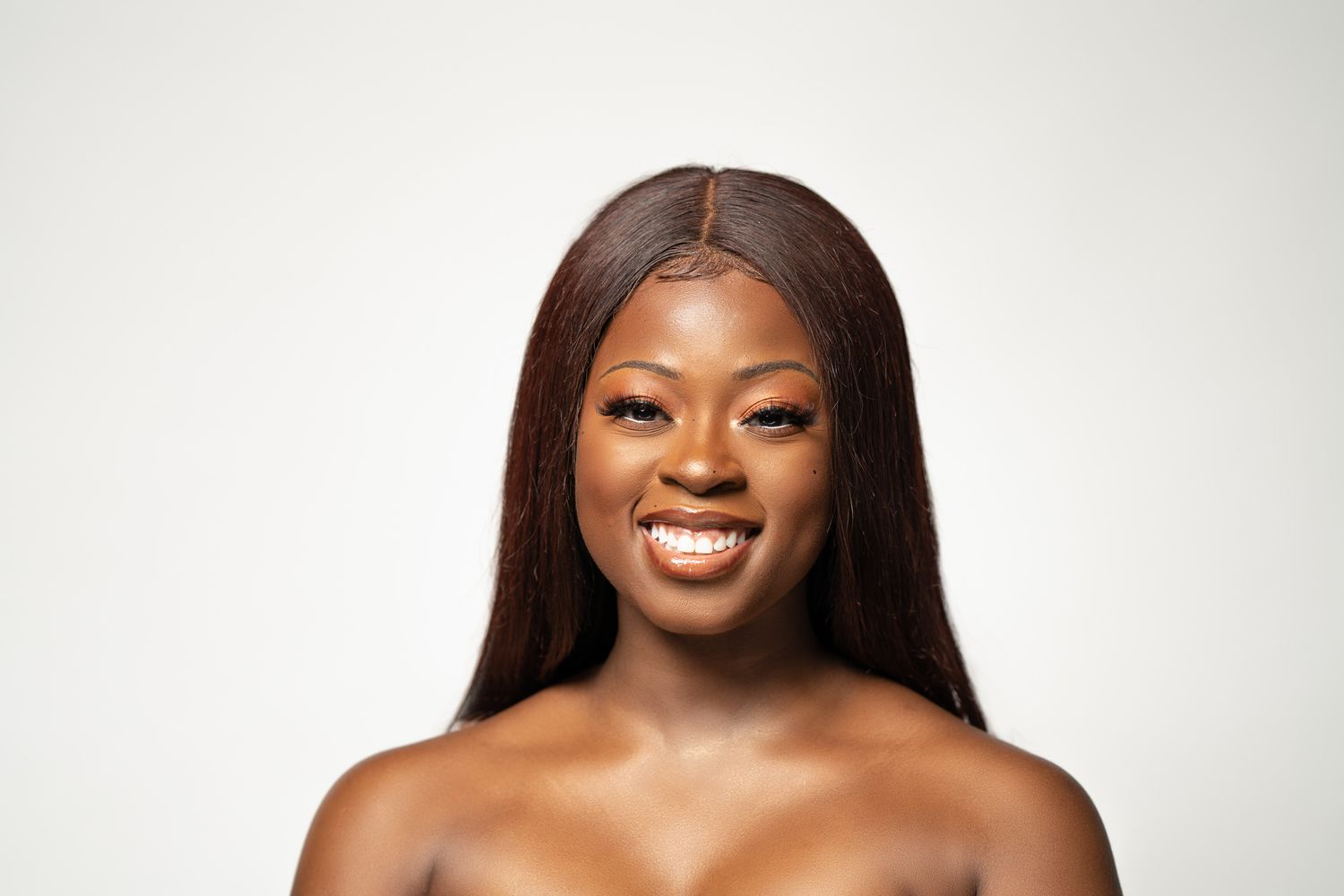 Portrait against white background showing bright smile and long straight hair.
