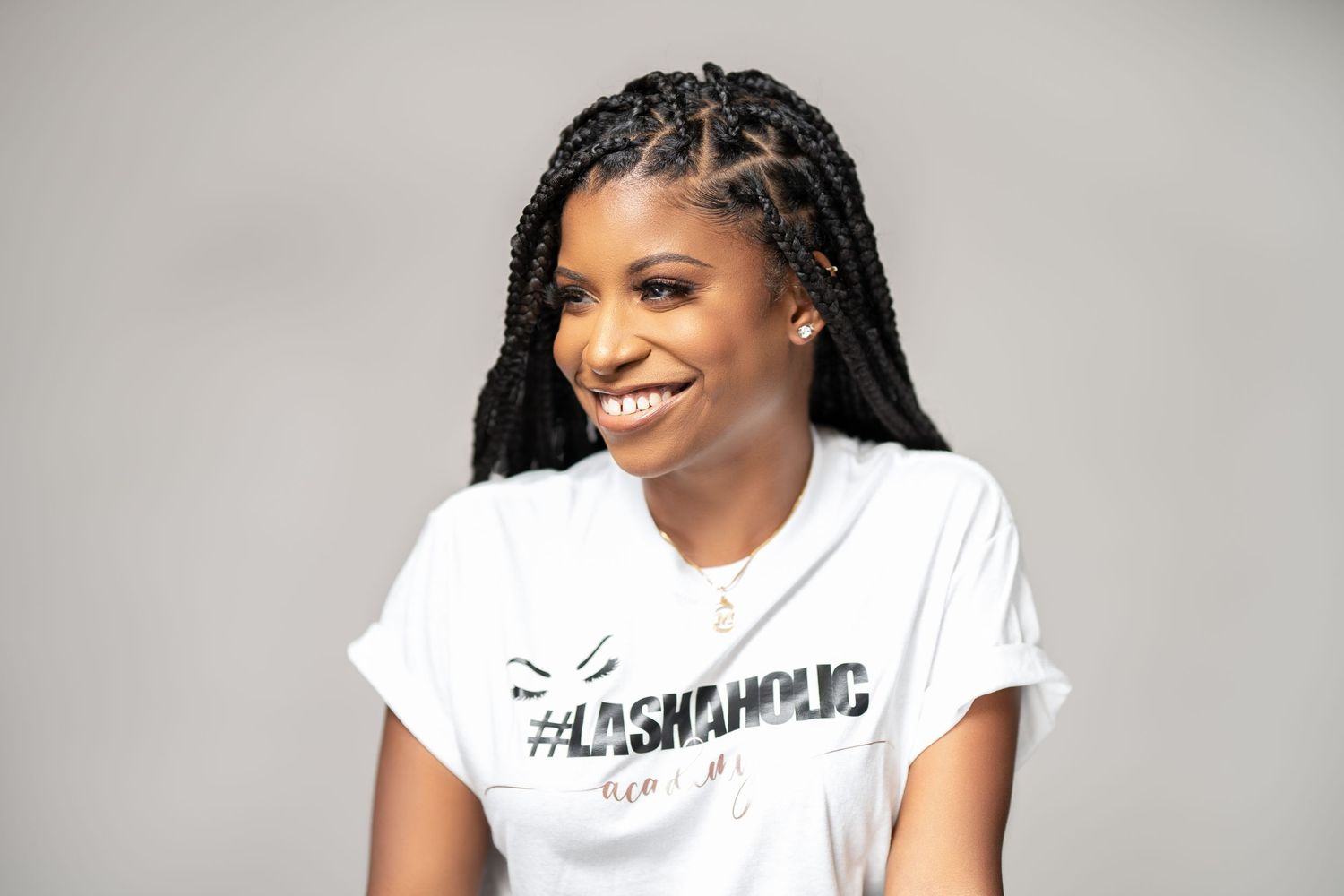 Joyful expression with braided hairstyle wearing fashionable hashtag t-shirt against grey backdrop.