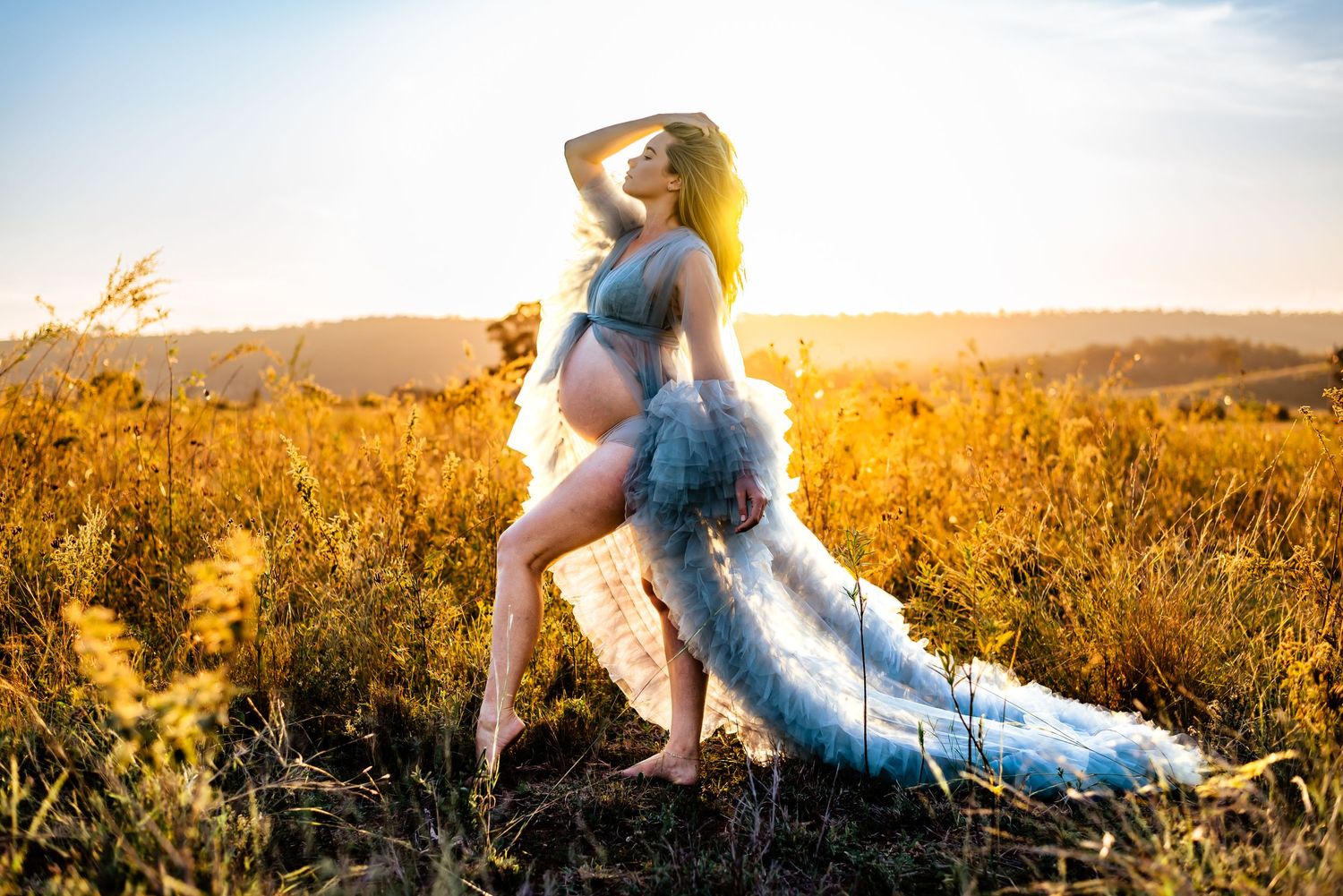 A graceful maternity portrait in a blue dress with flowing train against golden wildflowers.