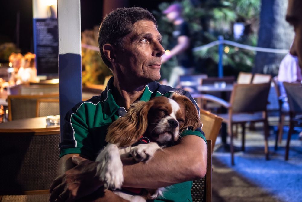 Man holds sleeping puppy in neon lit patio.