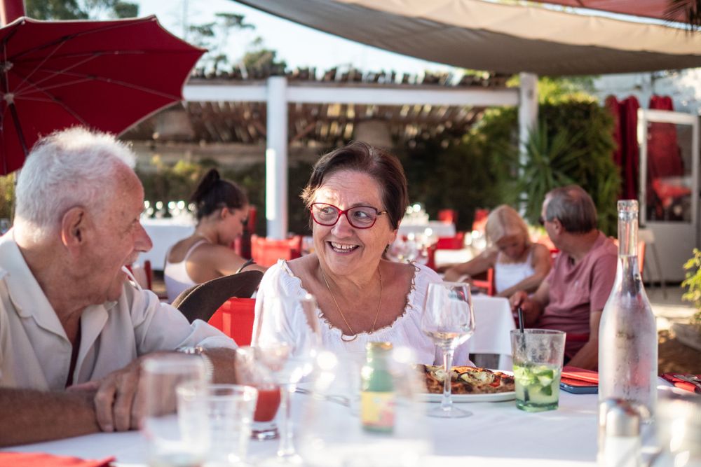 Elderly woman smiles at husband on eccentric patio in Southern France.