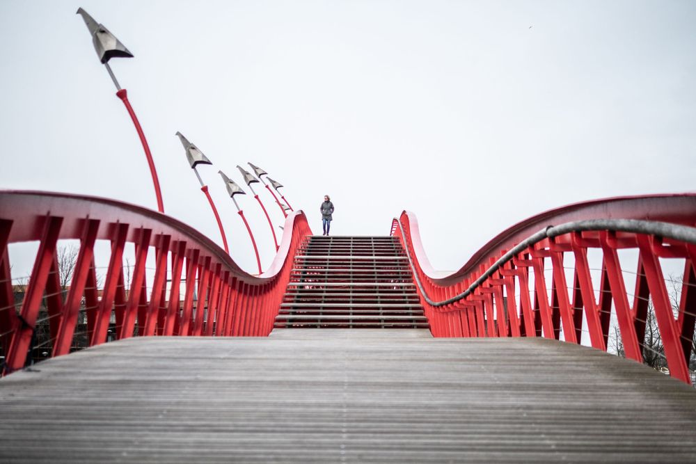 Lone woman crosses bright red bridge in Amsterdam.