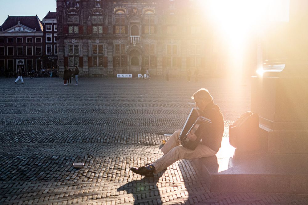 Man playing accordion lit up with beaming sunlight in Delft main square.