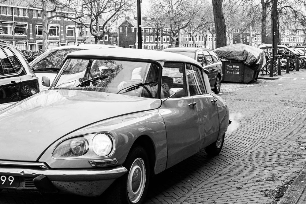 Black and white photo of man driving old car in the streets of Delft.