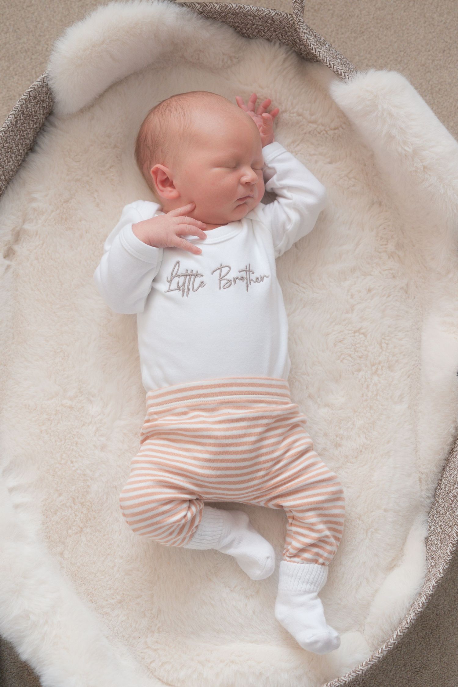 A newborn baby laying on a soft blanket within a baby basket. Neutral colours.