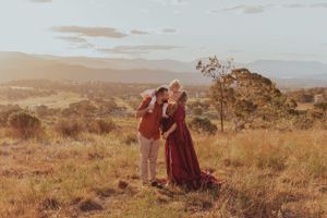 Couple in formal attire standing on hilltop during golden hour.