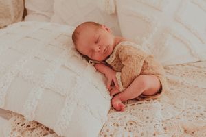 Peaceful sleeping newborn baby swaddled in soft beige blanket resting on white textured bedding.