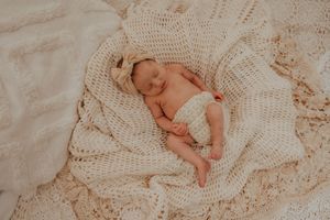 Sleeping newborn baby in cream crochet blanket and headband, peaceful nursery photo.