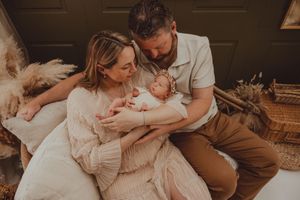 A couple sits together cradling their newborn baby in a warm, boho-styled newborn photography session.