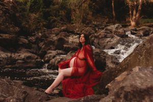 Person in red flowing dress posing near rocky waterfall.
